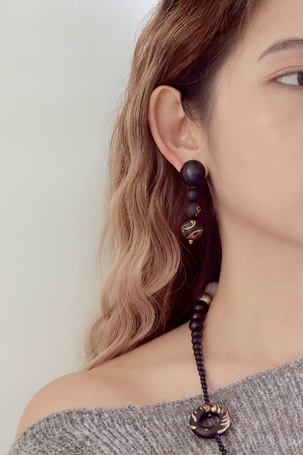 Plum Blossom Lacquer Quasi-Maki-e Long Earrings — Close-up of a person wearing a black beaded earring with a gold clasp.
