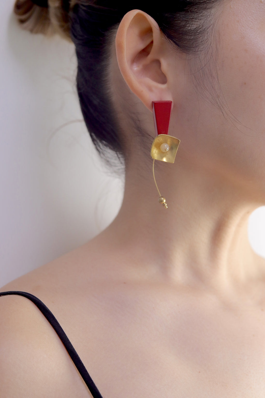Red Hibiscus Lacquer Quasi-Maki-e Earrings — Close-up of a person wearing a gold earring with a red accent on a neutral