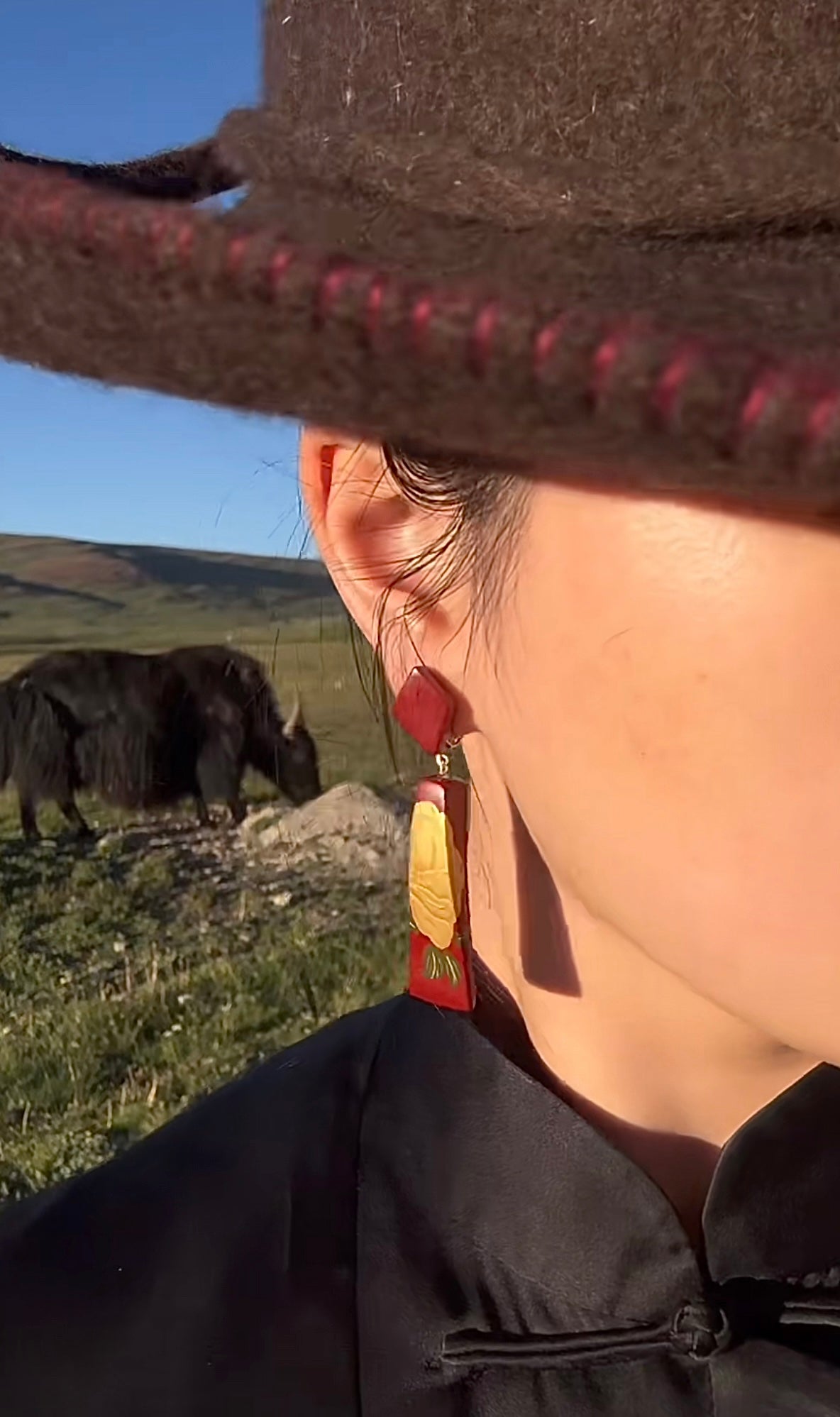 Red Peony Lacquer Quasi-Maki-e Earrings — Person wearing a brown hat with red trim and earrings, standing in a field with a