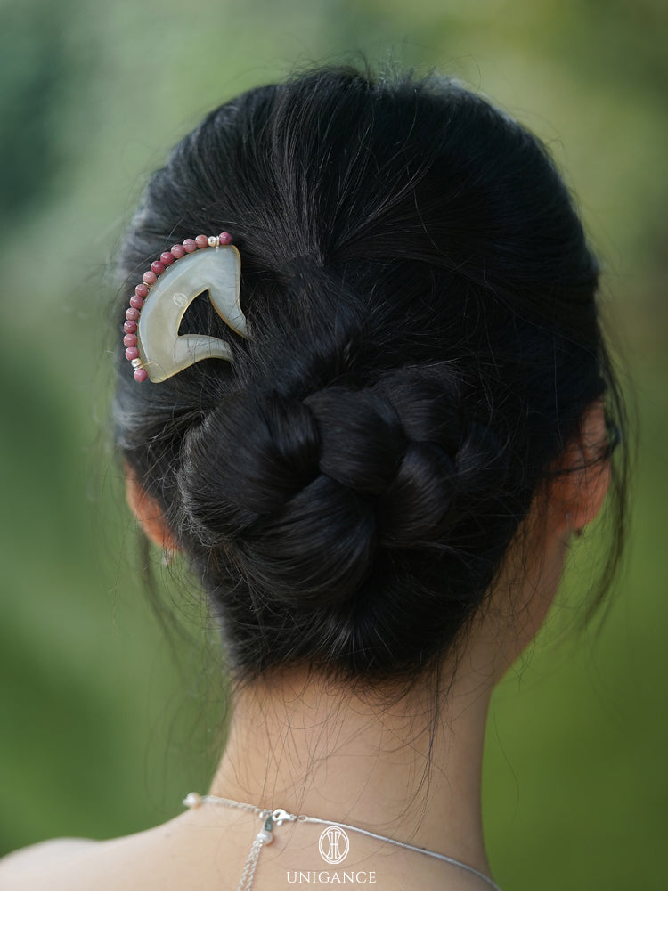 Person with intricately styled hair featuring a decorative hairpin against a blurred green background