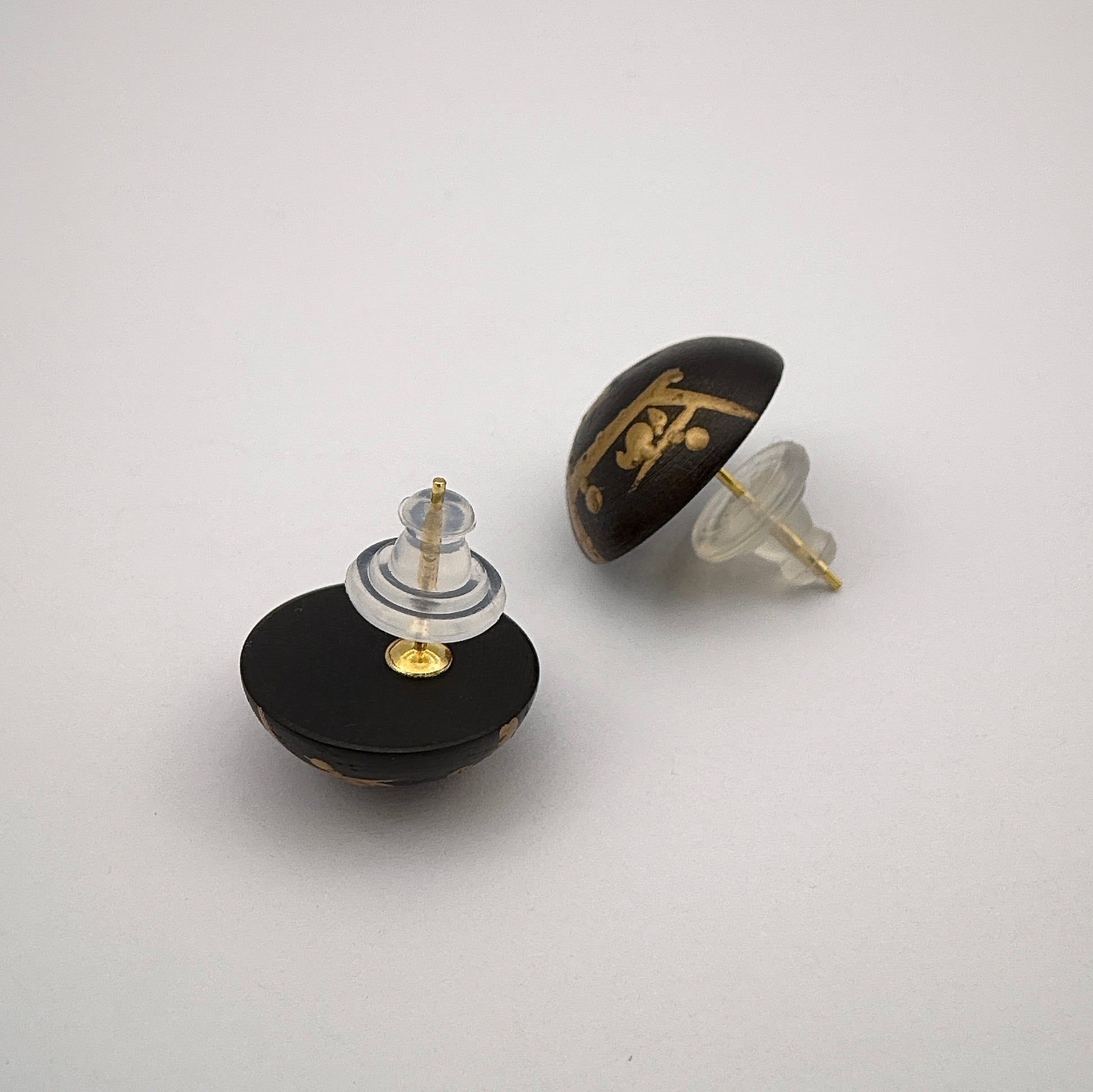 Two black and gold earrings on a light gray background