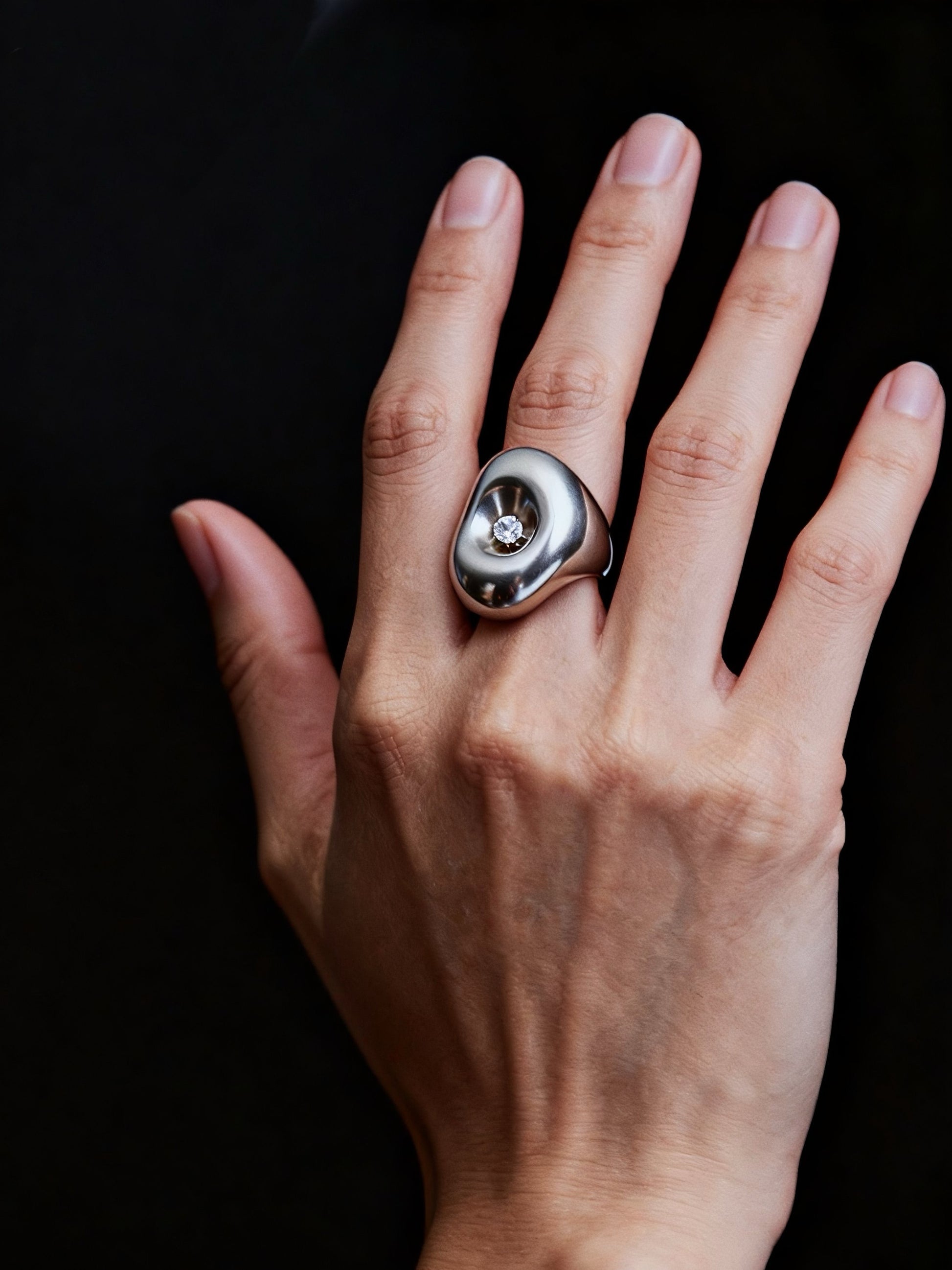 Hand wearing a silver ring with a dark background