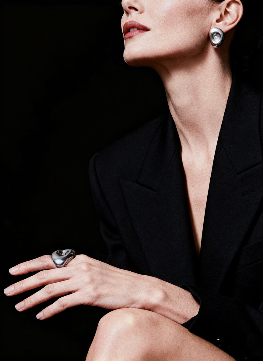 Woman wearing a black outfit with jewelry including earrings and a ring, against a dark background.