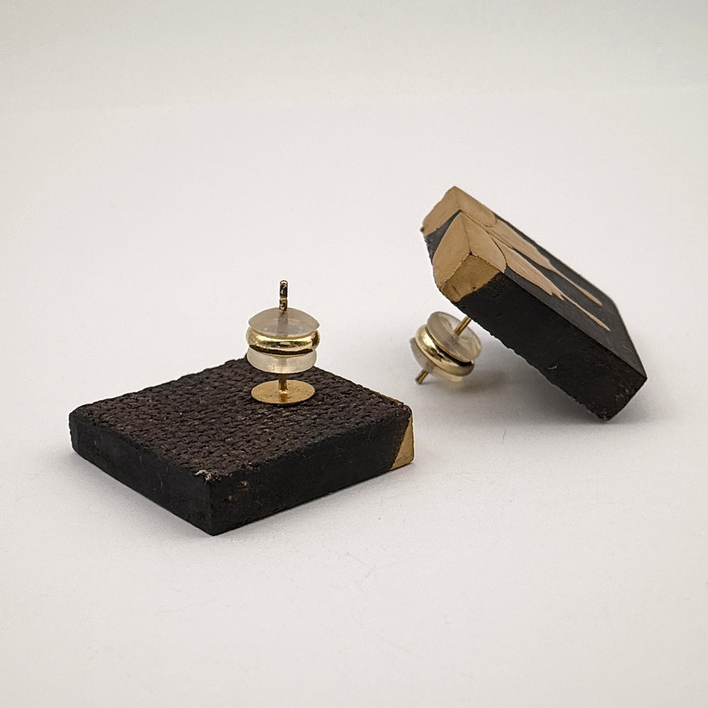 Secret Flower Lacquer Quasi-Maki-e Earrings — Black square pincushion with gold-colored pins on a white background