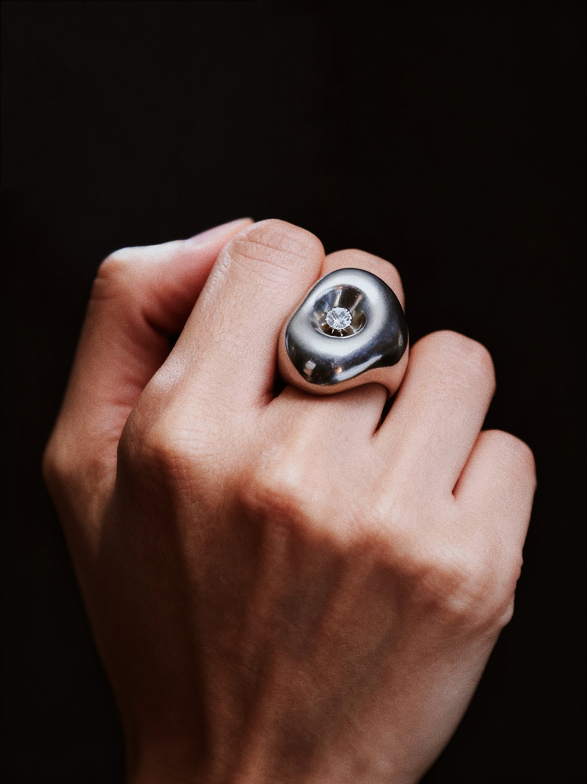 Hand wearing a silver ring with a diamond on a black background