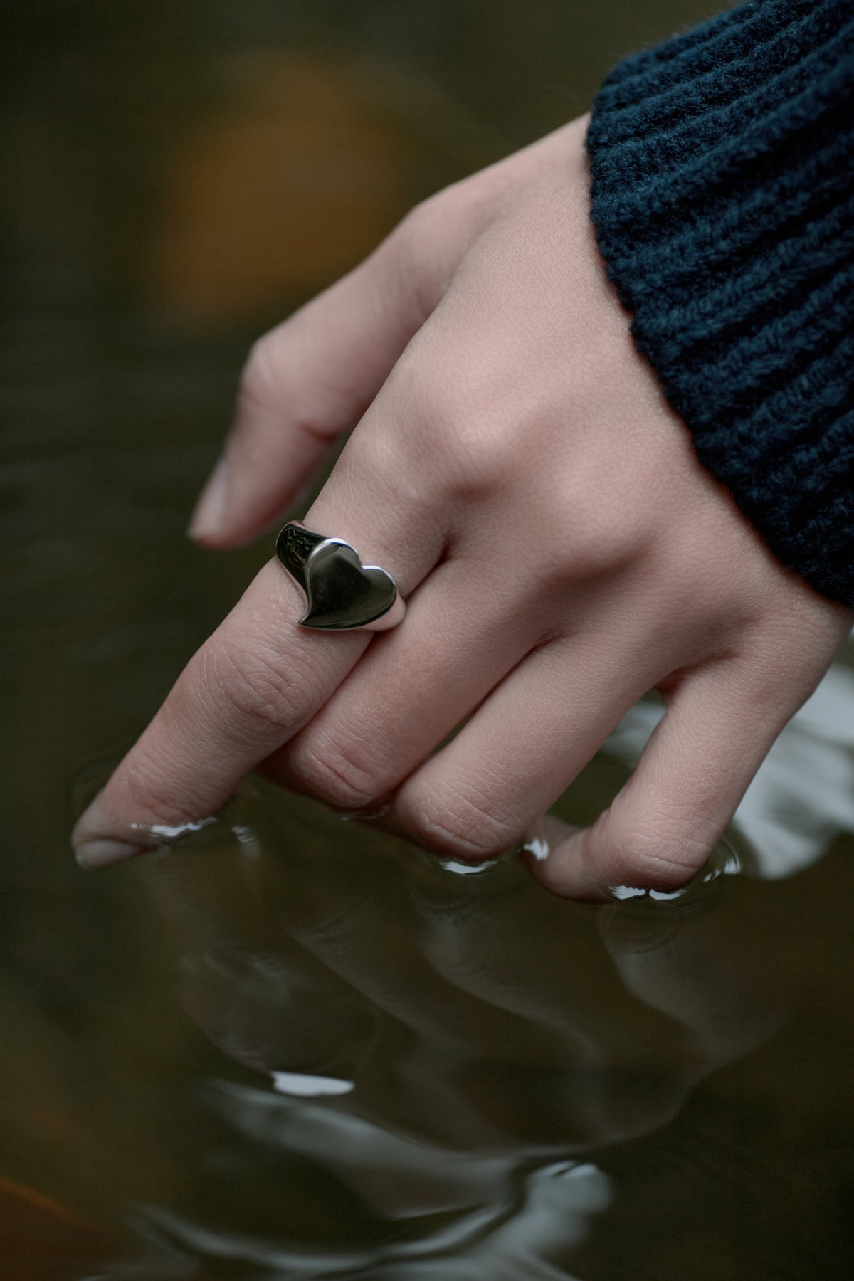 Silver Heart Signet Ring — Hand with a heart-shaped ring on a blurred water background