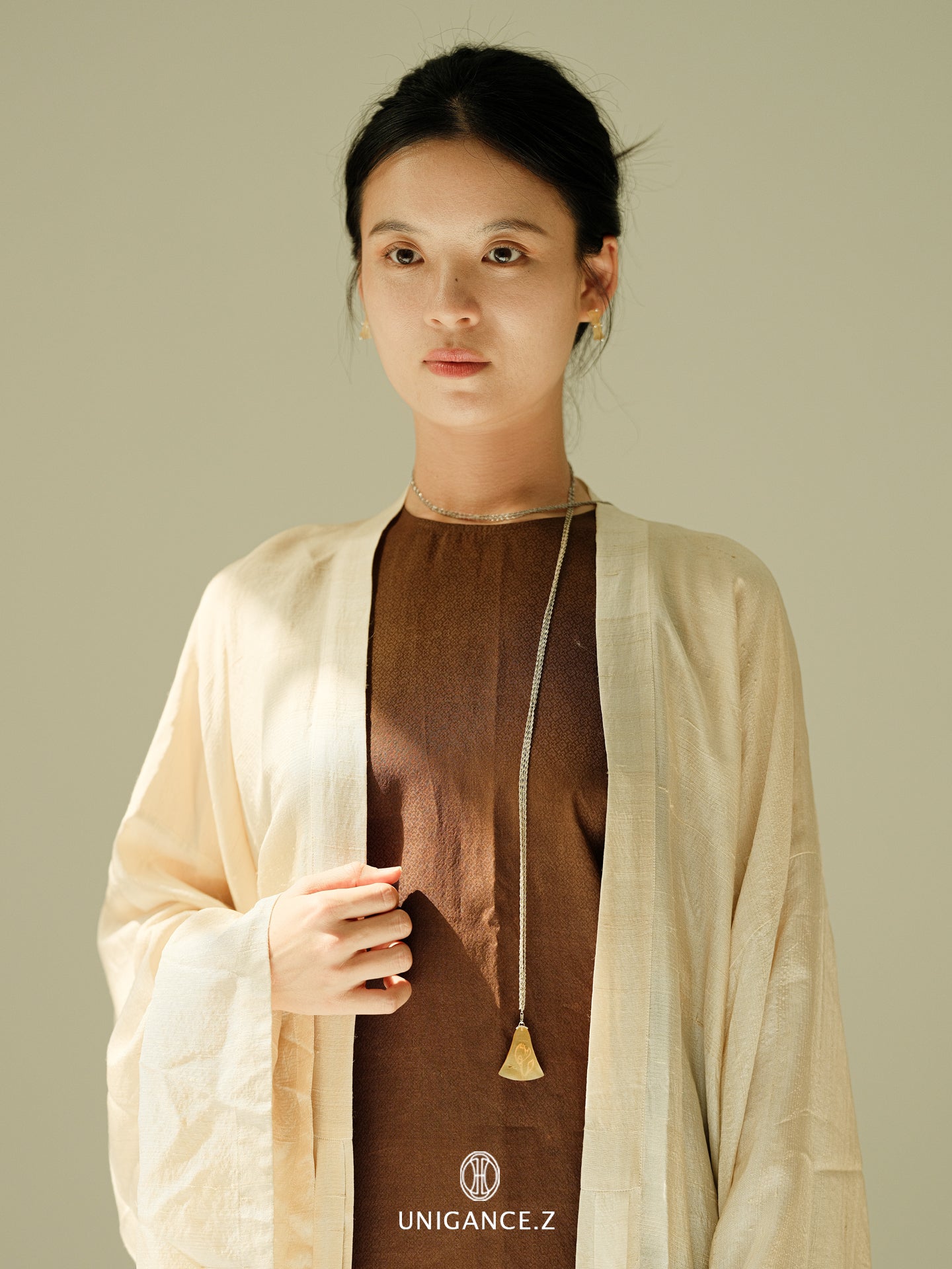 Woman wearing a beige cardigan over a brown top with a visible brand logo on a plain background