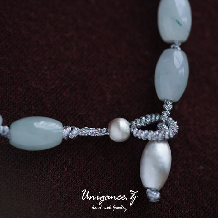 Beaded necklace with green and white beads on a dark brown background, featuring the brand 'Unigance'.