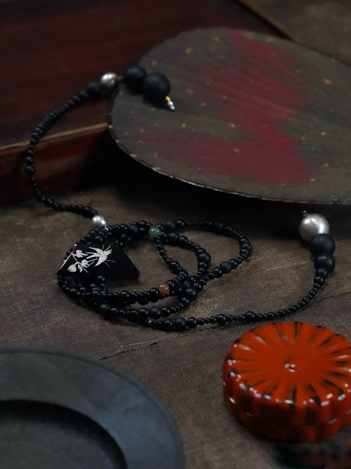 Snow Sparrow Lacquer Quasi-Maki-e Long Lariat Necklace — Black beaded necklace with a pendant on a textured surface