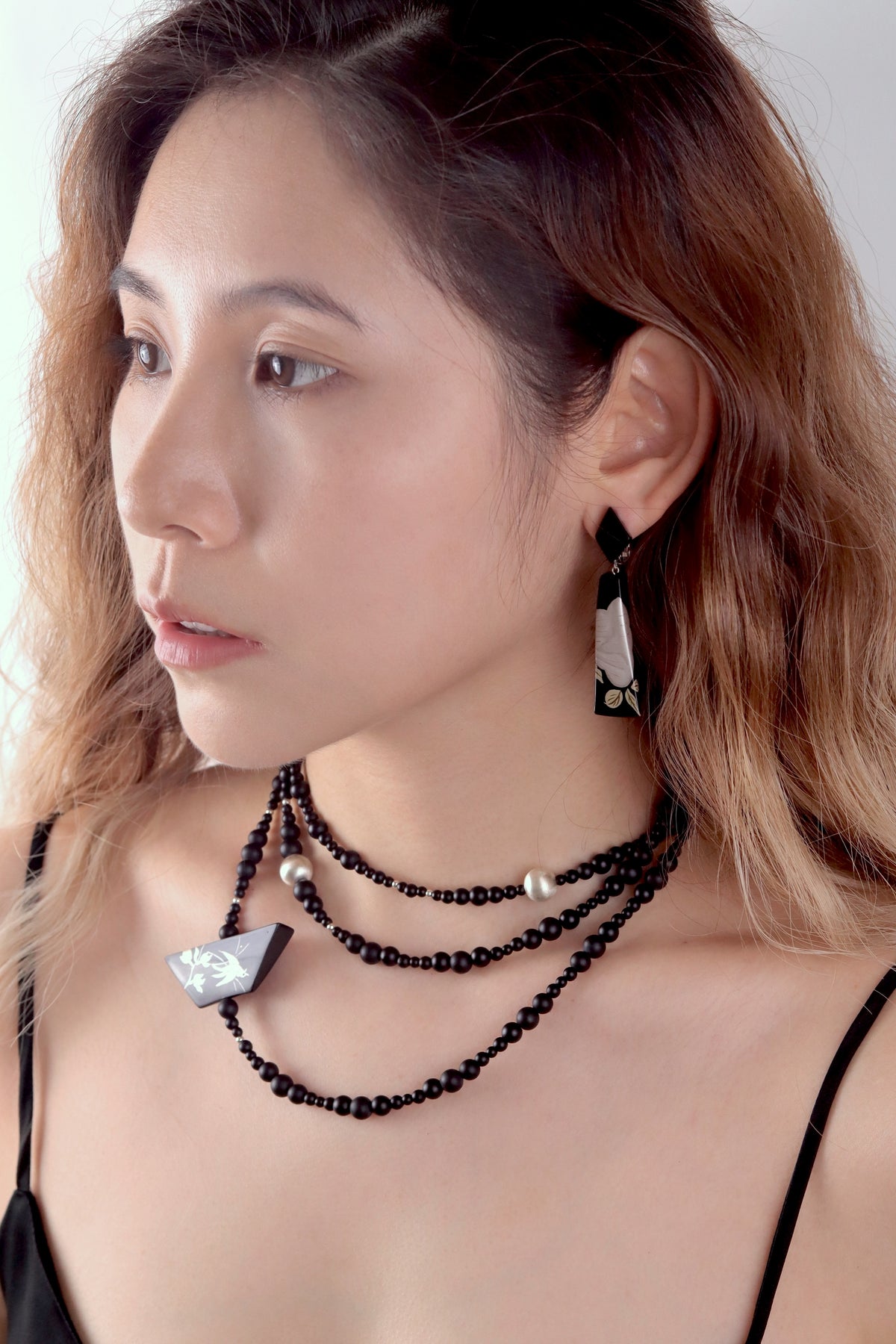Snow Sparrow Lacquer Quasi-Maki-e Long Lariat Necklace — Woman wearing a black beaded necklace and earrings against a neutral