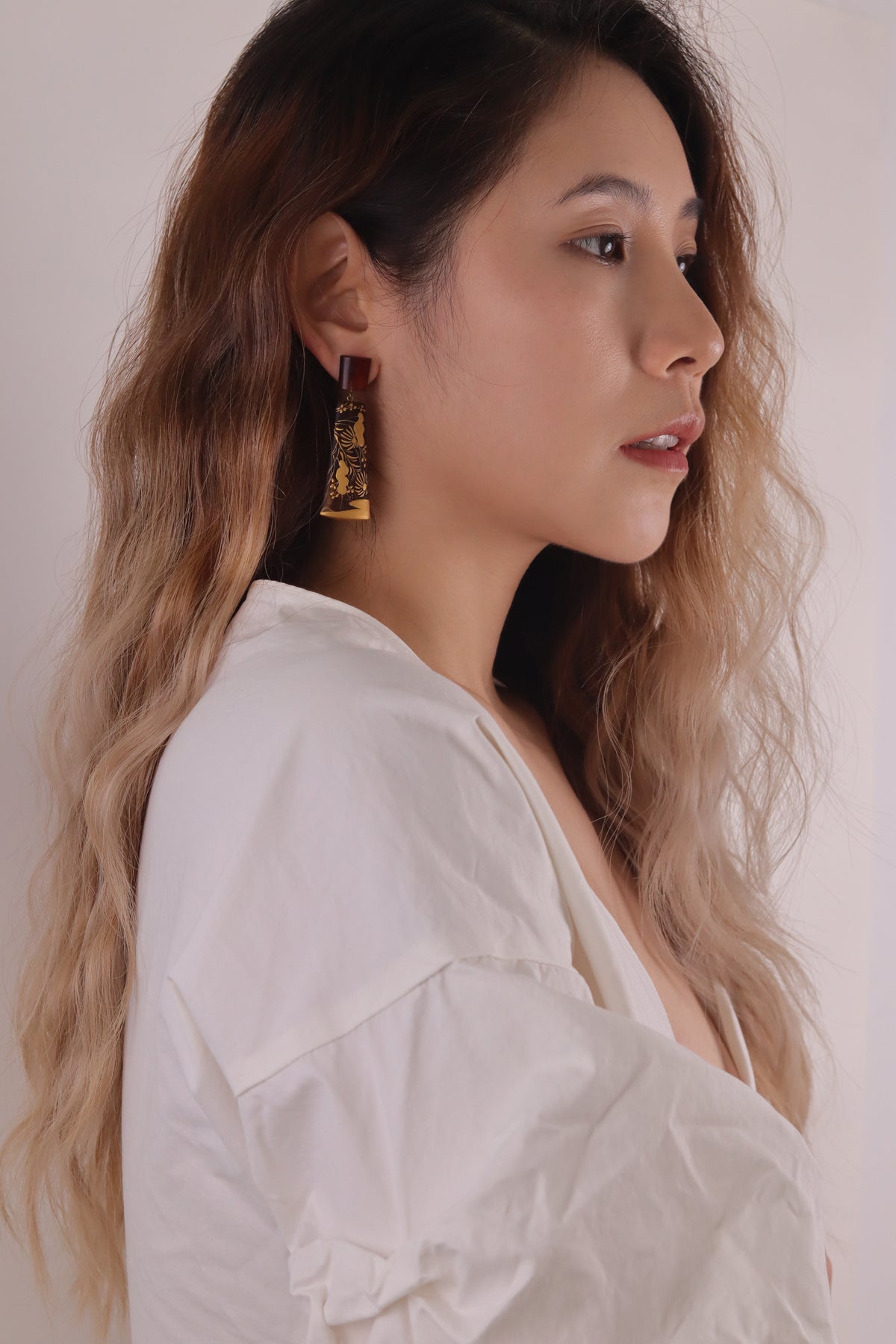 Sunset Watergrass Lacquer Quasi-Maki-e Earrings — Woman wearing gold earrings with a plain background