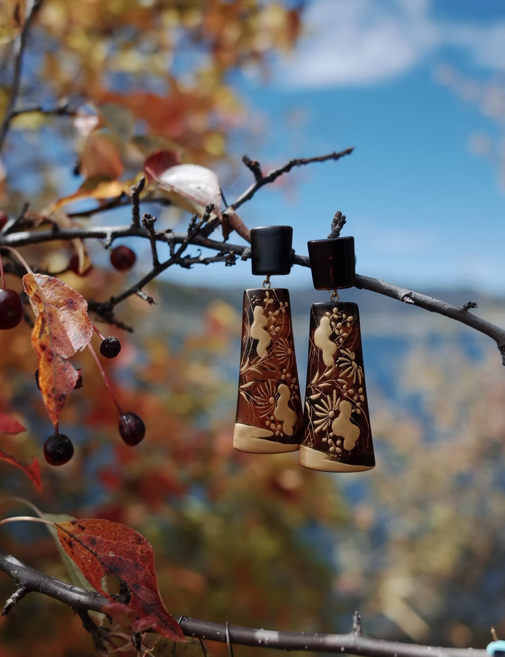 Sunset Watergrass Lacquer Quasi-Maki-e Earrings — Pair of earrings with deer design hanging on a branch with autumn leaves.