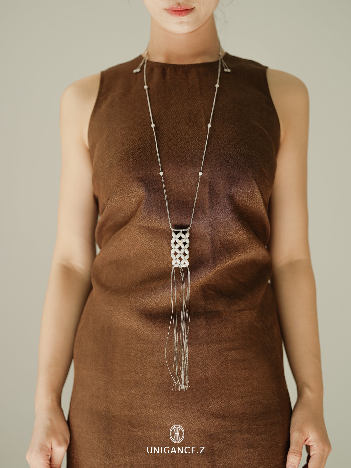 Person wearing a long necklace with a neutral background, featuring the brand 'UNIGANCE.Z'.