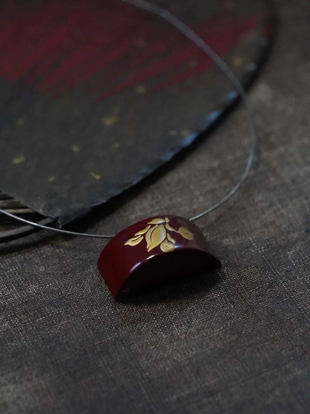 Tranquil Magnolia Lacquer Quasi-Maki-e Necklace — Brown pendant with gold design on a dark fabric background