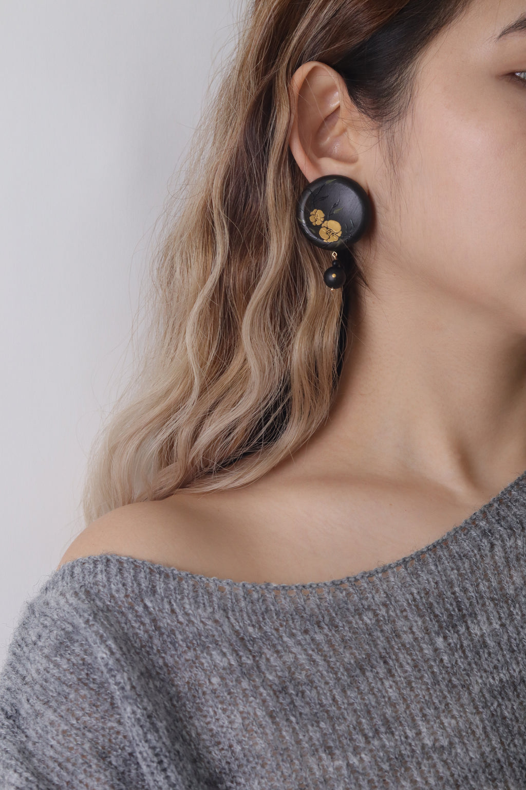 Twin Blossoms Black Lacquer Drop Earrings — Close-up of a person wearing a black earring with gold accents on a plain