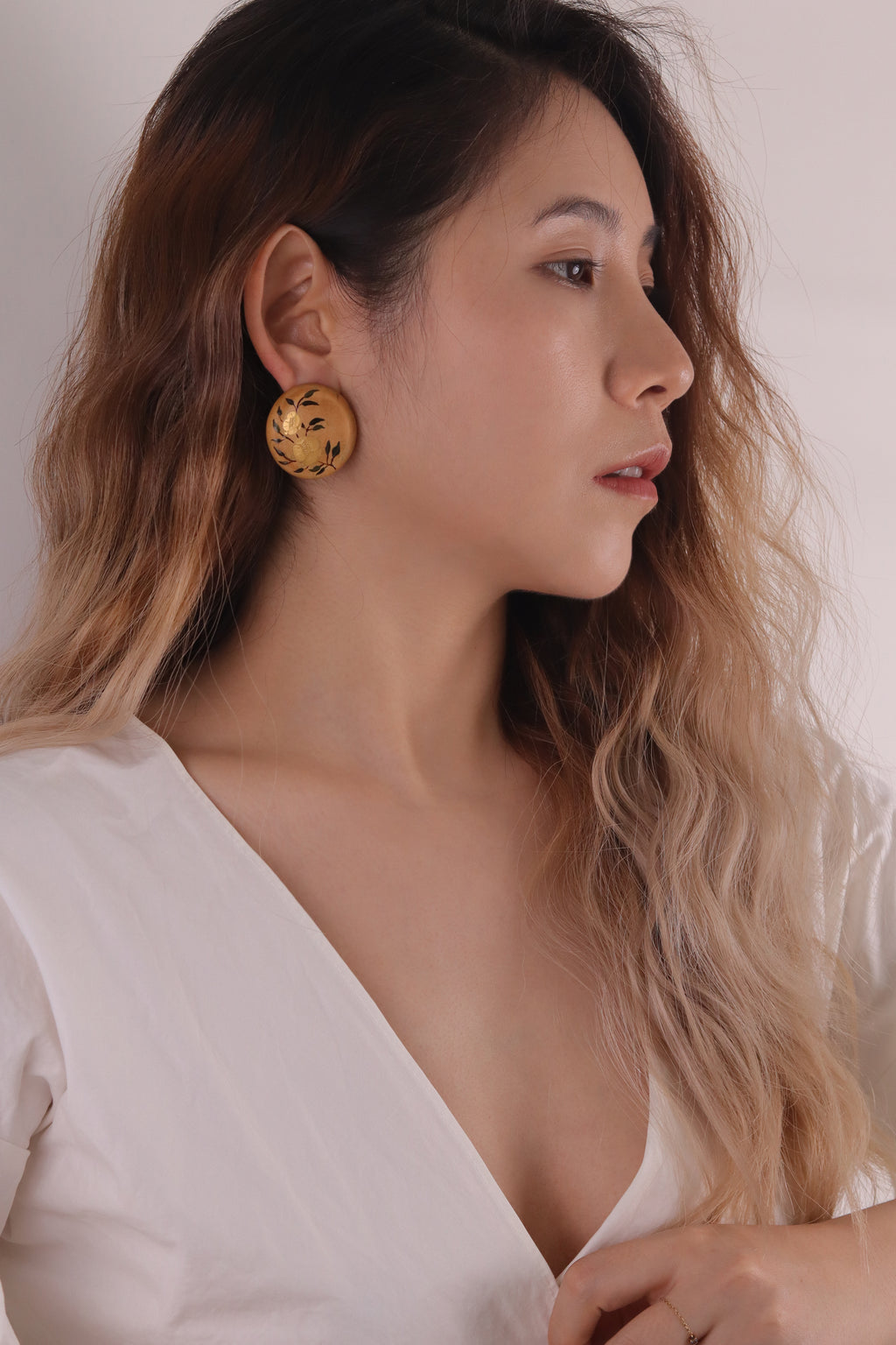 Twin Blossoms Natural Lacquer Earrings — Woman wearing gold earrings with a plain background