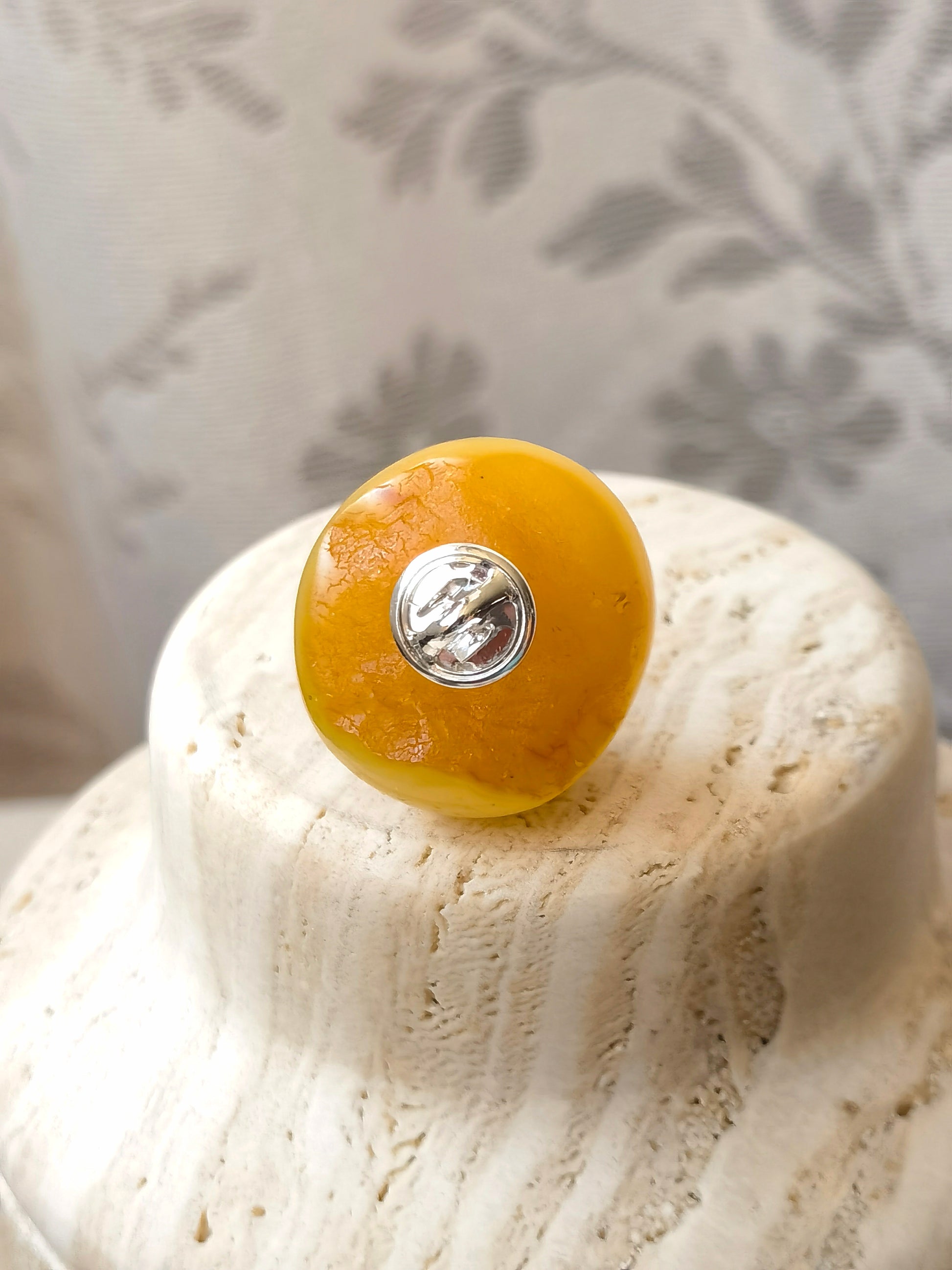Close-up of a yellow knob on a textured white surface with a blurred floral-patterned background.